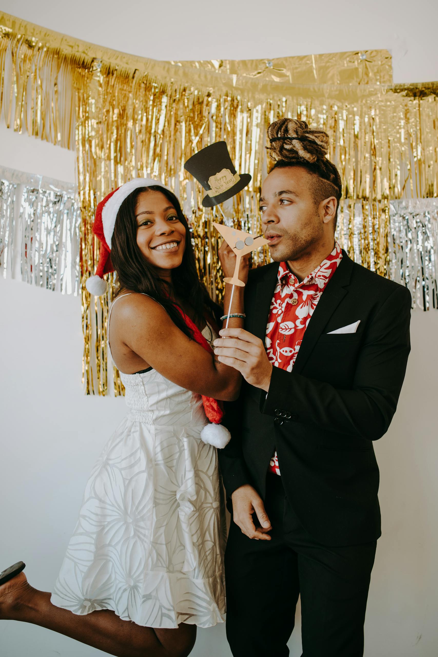 A cheerful couple celebrates a holiday party with festive decorations and props.