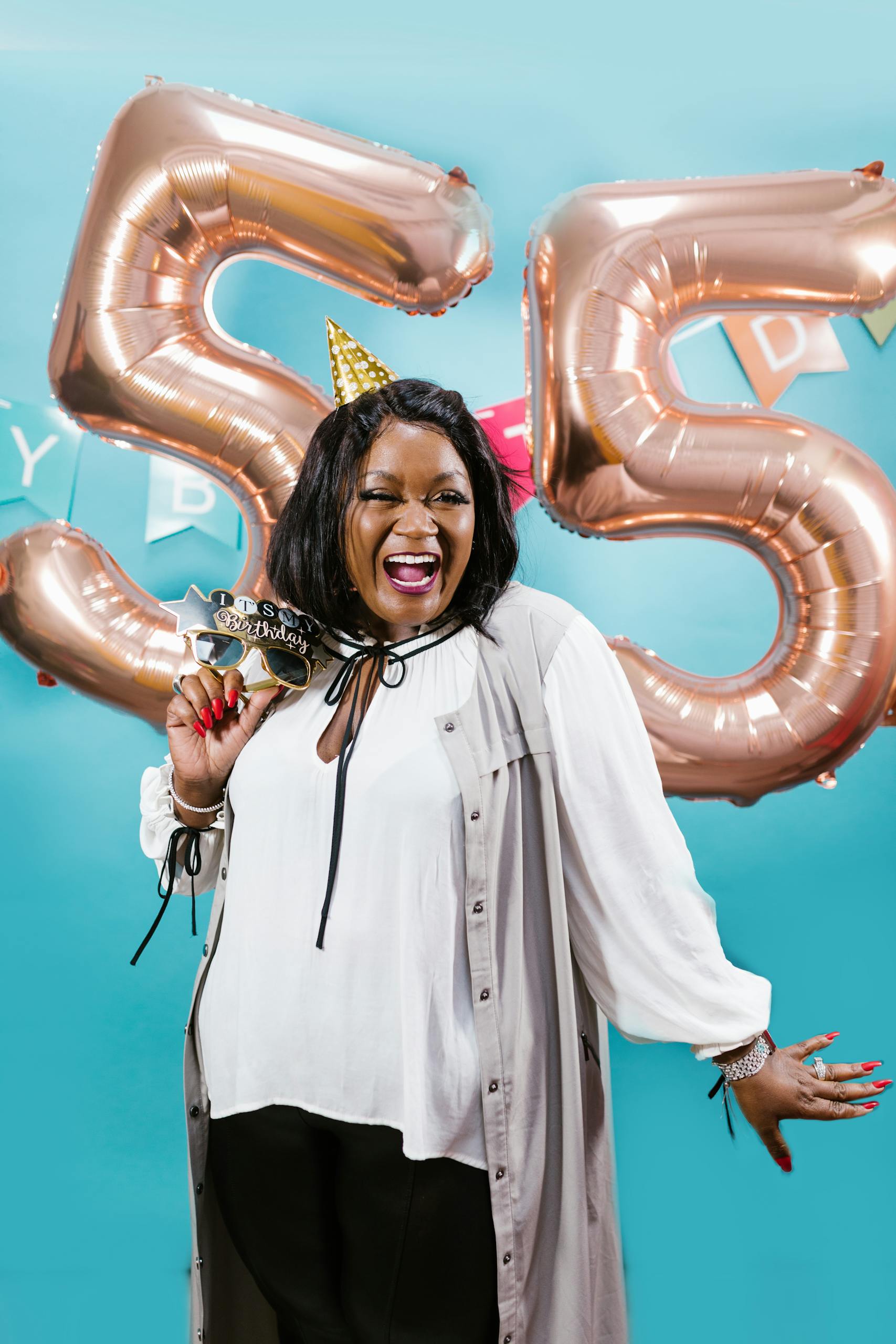 Energetic woman celebrating her 55th birthday with festive balloons and fun props.